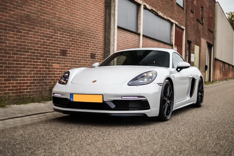 Vooraanzicht van de Porsche 718 Cayman bij een bakstenen muur